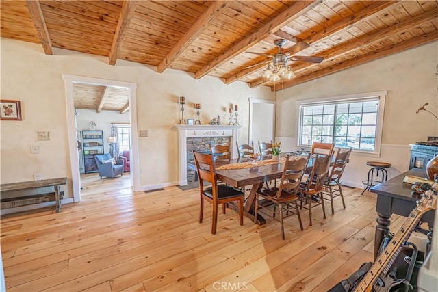 dining room featuring beam ceiling, light wood-style floors, wood ceiling, a stone fireplace, and baseboards