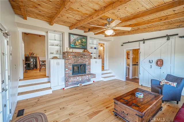 living room with a barn door, wooden ceiling, hardwood / wood-style floors, built in shelves, and beam ceiling