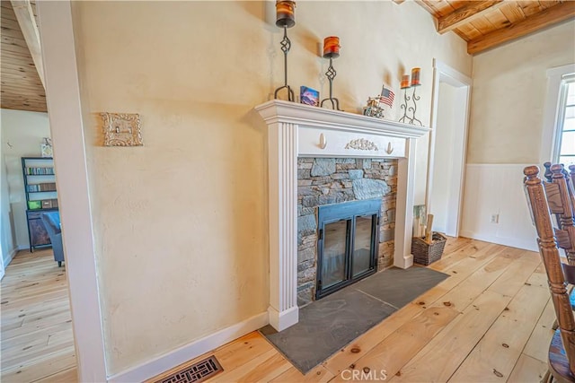 details with visible vents, a wainscoted wall, a stone fireplace, and wood finished floors