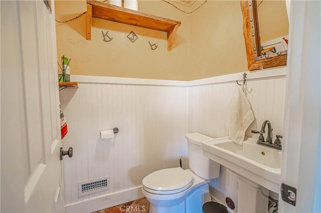 half bath with toilet, wainscoting, a sink, and visible vents