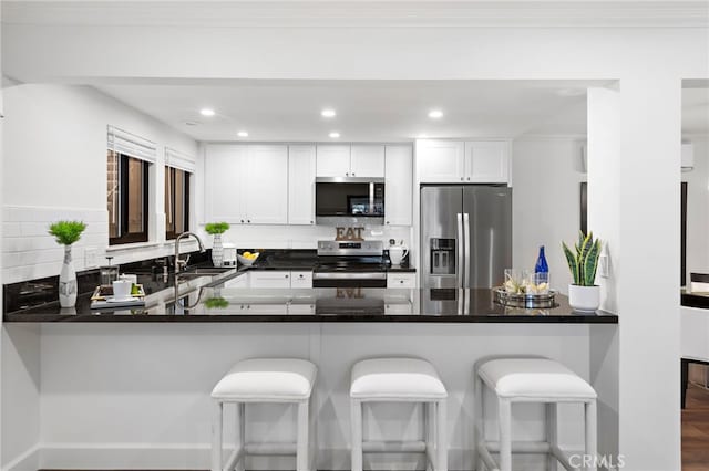 kitchen with a peninsula, a sink, stainless steel appliances, white cabinetry, and backsplash