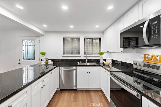 kitchen featuring light wood finished floors, appliances with stainless steel finishes, white cabinets, a sink, and dark stone countertops