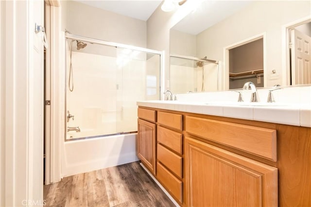 full bath with double vanity, combined bath / shower with glass door, a sink, and wood finished floors