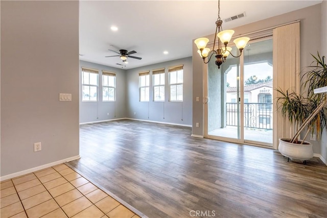 spare room with ceiling fan with notable chandelier, visible vents, baseboards, and wood finished floors