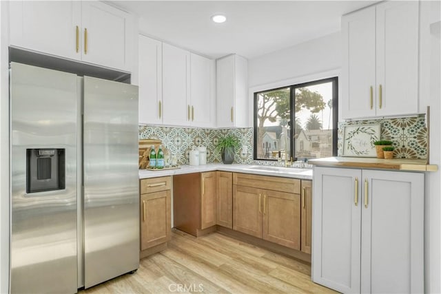 kitchen with light countertops, stainless steel fridge with ice dispenser, light wood-style flooring, and decorative backsplash