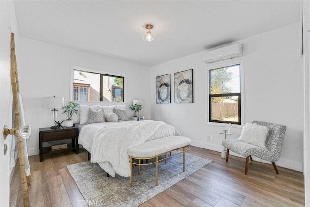 bedroom with a wall mounted air conditioner, multiple windows, and light wood-style floors