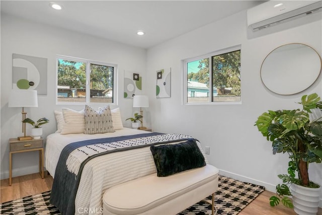 bedroom featuring a wall mounted air conditioner, baseboards, wood finished floors, and multiple windows