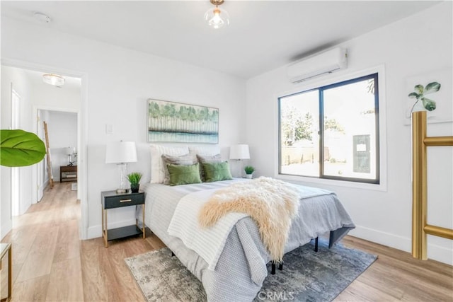 bedroom with baseboards, wood finished floors, and an AC wall unit