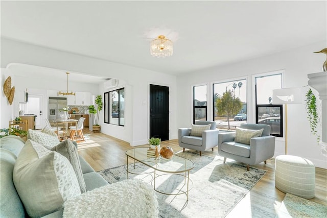 living area with baseboards, a notable chandelier, a wall unit AC, and light wood-style floors