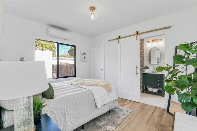 bedroom with a barn door, a wall mounted AC, and light wood-style floors
