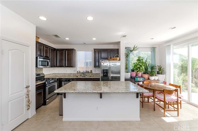 kitchen featuring a center island, stainless steel appliances, visible vents, dark brown cabinetry, and light stone countertops