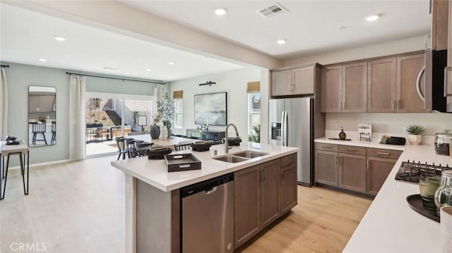 kitchen featuring stainless steel appliances, light countertops, visible vents, a kitchen island with sink, and a sink