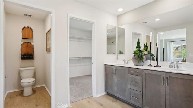 full bath with double vanity, visible vents, toilet, wood finished floors, and a sink