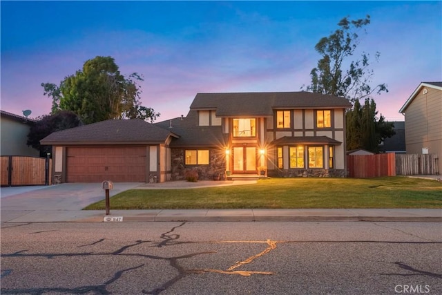 tudor-style house featuring driveway, a gate, fence, a yard, and an attached garage