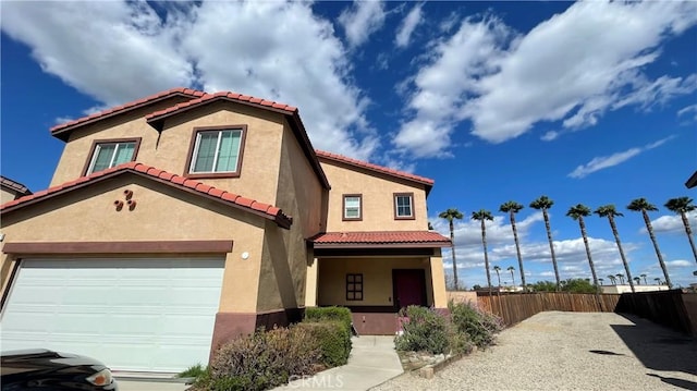 mediterranean / spanish home featuring stucco siding, an attached garage, a tile roof, and fence