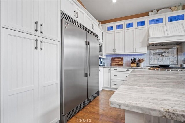 kitchen featuring built in appliances, wood finished floors, white cabinetry, and decorative backsplash