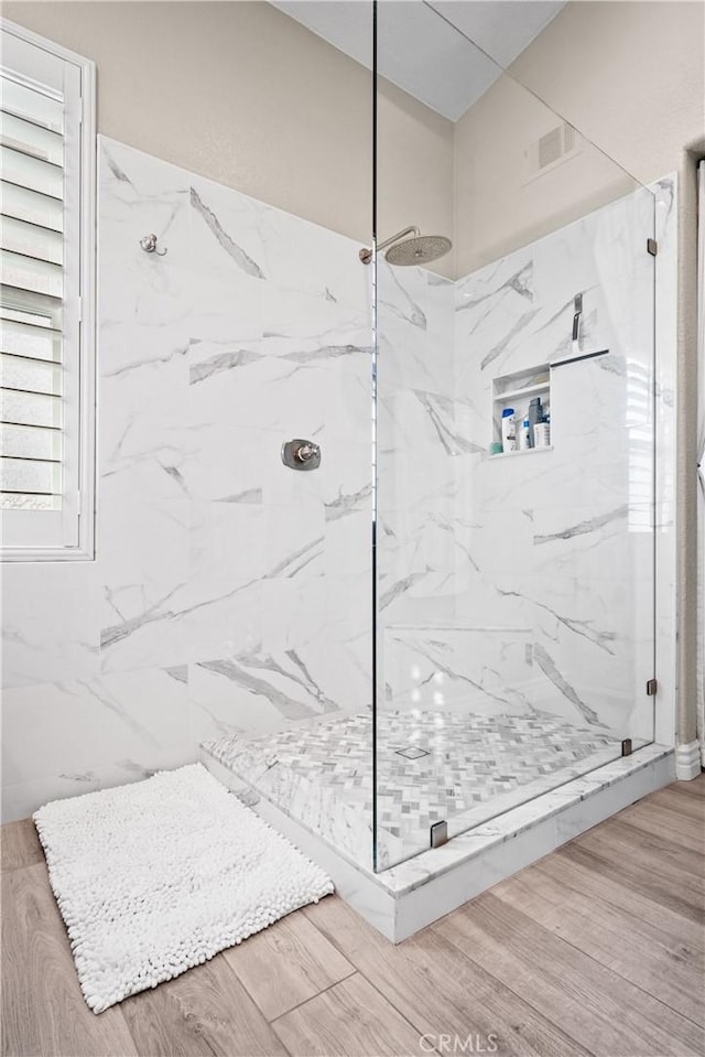 bathroom with wood finished floors, a marble finish shower, and visible vents