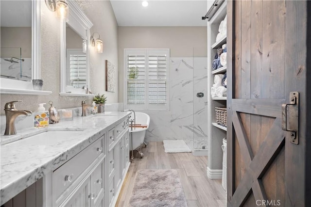 bathroom featuring double vanity, a marble finish shower, wood finished floors, a freestanding tub, and a sink