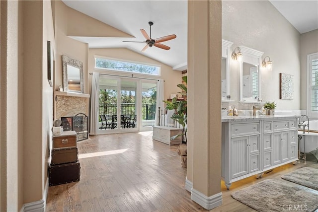 interior space featuring a fireplace, a ceiling fan, vaulted ceiling, double vanity, and wood-type flooring