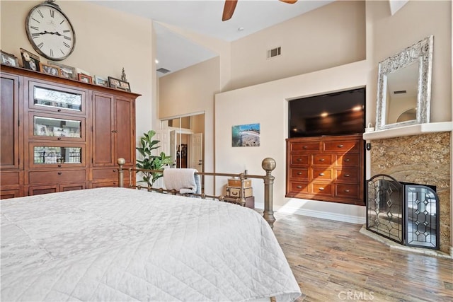 bedroom featuring baseboards, visible vents, a glass covered fireplace, a towering ceiling, and wood finished floors