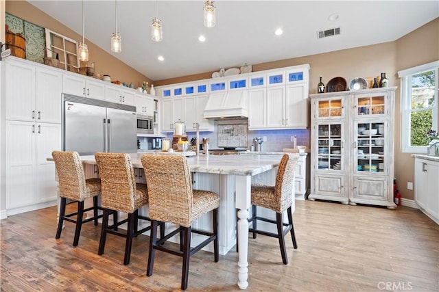 kitchen featuring visible vents, white cabinets, light wood-style floors, backsplash, and custom exhaust hood