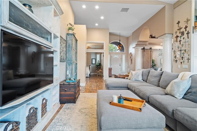 living area with decorative columns, visible vents, wood finished floors, a high ceiling, and recessed lighting