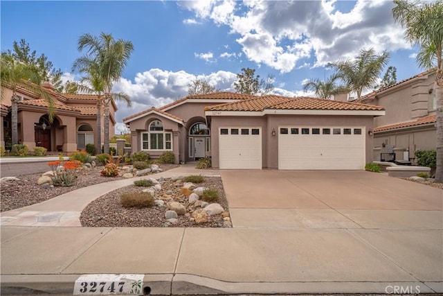 mediterranean / spanish-style home with a garage, concrete driveway, a tiled roof, and stucco siding