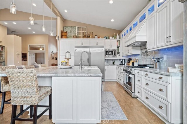 kitchen featuring backsplash, white cabinetry, vaulted ceiling, built in appliances, and light wood-type flooring