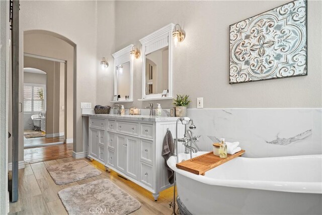 bathroom featuring double vanity, a freestanding bath, and wood finished floors