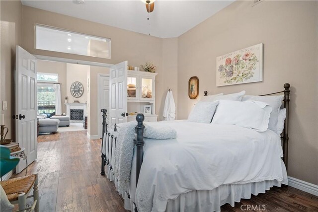 bedroom with wood-type flooring, a fireplace, and baseboards