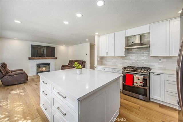 kitchen featuring open floor plan, double oven range, light wood-style flooring, and wall chimney exhaust hood