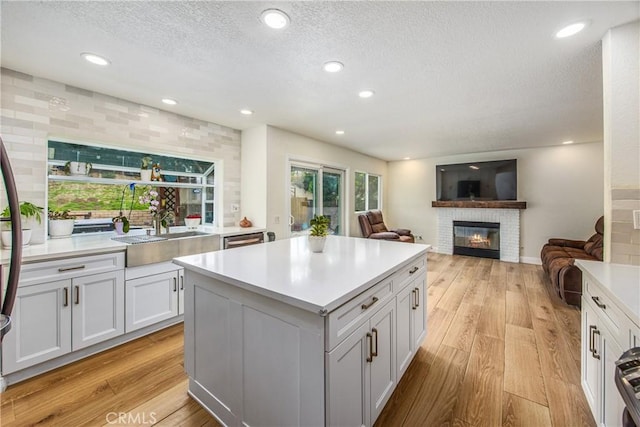 kitchen featuring light wood finished floors, a brick fireplace, light countertops, and a center island