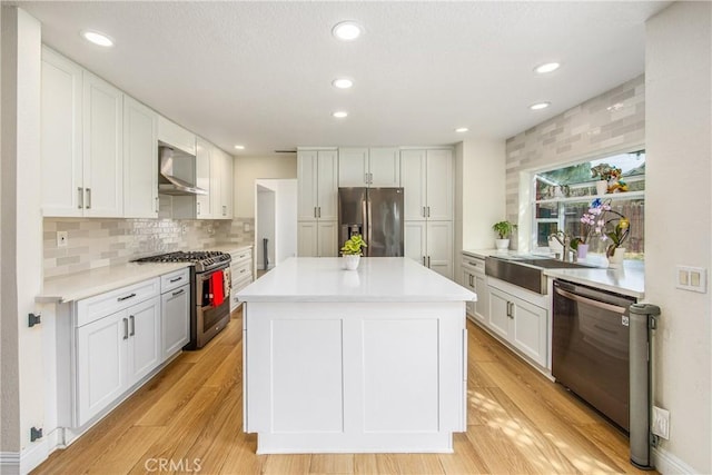 kitchen with stainless steel appliances, light wood-style floors, white cabinets, a sink, and wall chimney exhaust hood