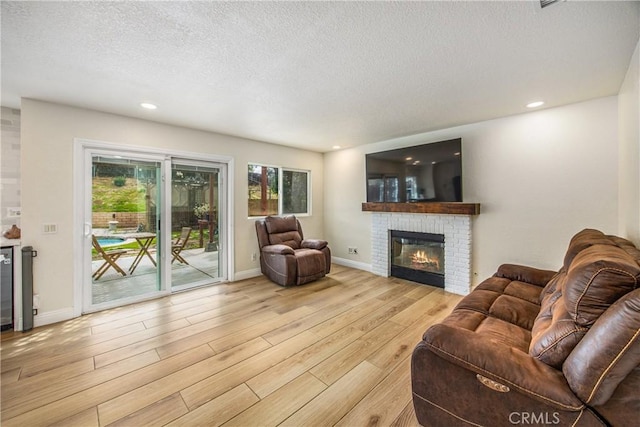 living room with a brick fireplace, a textured ceiling, baseboards, and wood finished floors