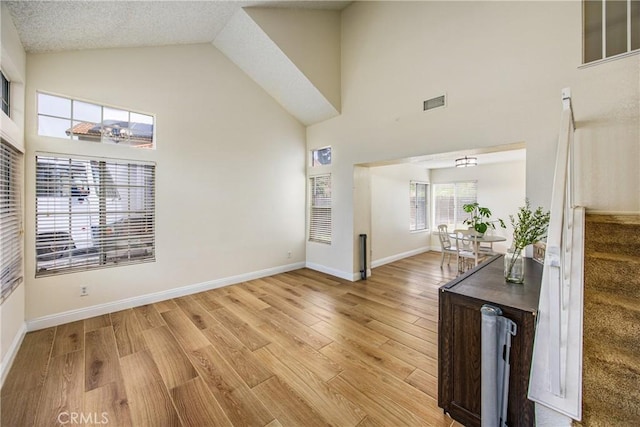 interior space with light wood finished floors, baseboards, visible vents, stairs, and high vaulted ceiling