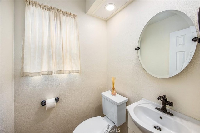 half bathroom with a textured wall, vanity, and toilet