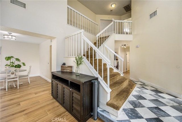 stairway featuring a towering ceiling, baseboards, visible vents, and tile patterned floors