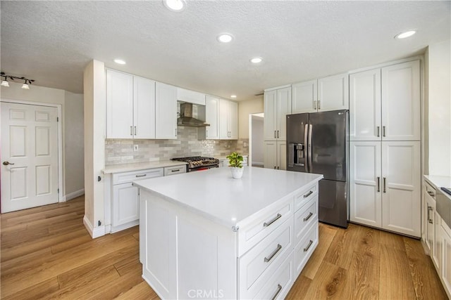 kitchen with light wood finished floors, white cabinets, stainless steel appliances, wall chimney range hood, and backsplash