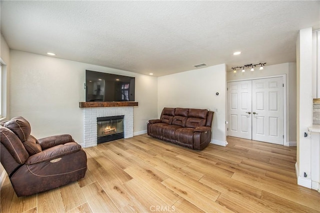 living area with a brick fireplace, light wood-style flooring, visible vents, and a textured ceiling