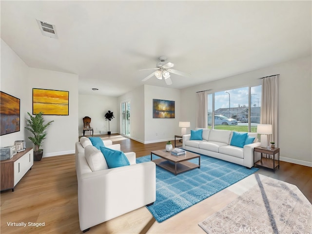 living area featuring baseboards, visible vents, ceiling fan, and wood finished floors