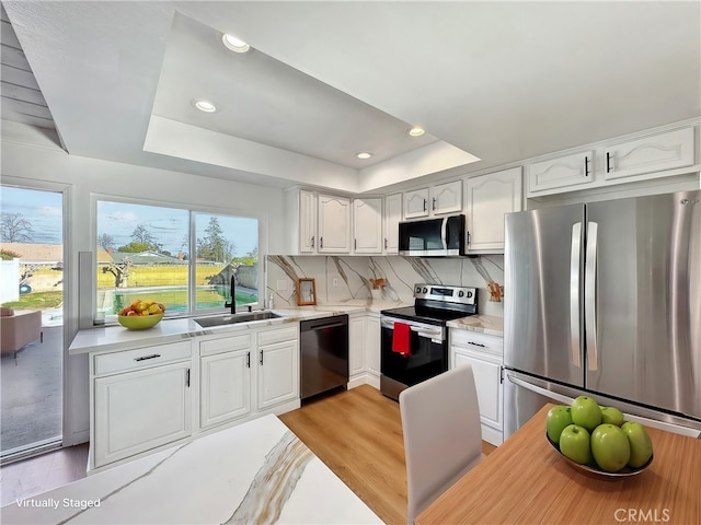 kitchen with tasteful backsplash, a raised ceiling, appliances with stainless steel finishes, white cabinetry, and a sink