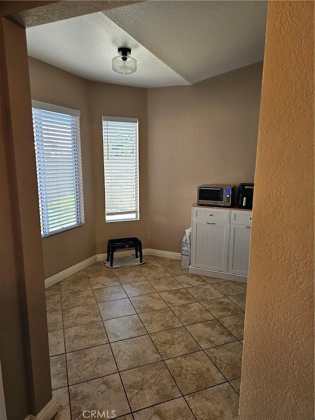 spare room with baseboards, a textured ceiling, light tile patterned flooring, and a healthy amount of sunlight