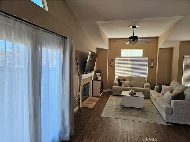 living room featuring dark wood-style floors, a fireplace, a ceiling fan, and baseboards