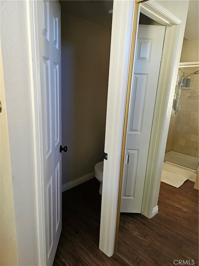 bathroom with toilet, a stall shower, baseboards, and wood finished floors