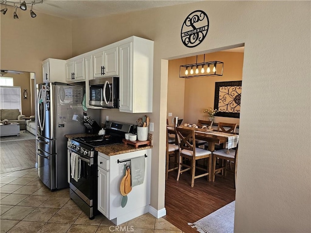 kitchen with light tile patterned floors, appliances with stainless steel finishes, dark stone countertops, white cabinetry, and high vaulted ceiling