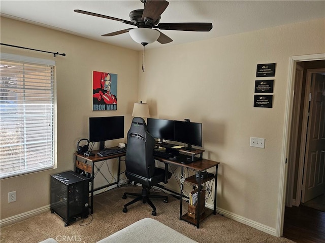 carpeted office space with a ceiling fan and baseboards