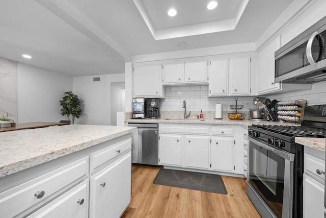 kitchen featuring light wood-style flooring, decorative backsplash, stainless steel appliances, and a sink