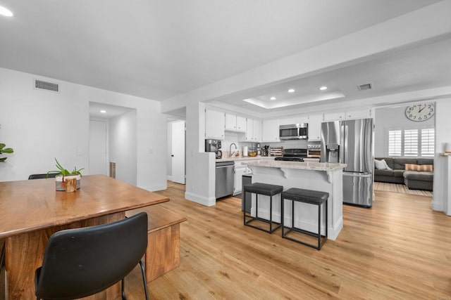 kitchen with visible vents, a raised ceiling, light wood-style flooring, a breakfast bar area, and stainless steel appliances