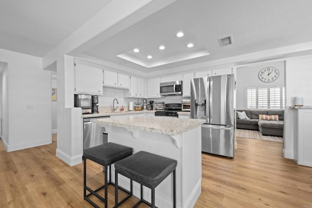 kitchen featuring visible vents, backsplash, a tray ceiling, stainless steel appliances, and a sink