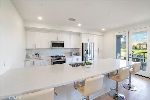 kitchen with visible vents, light wood-style floors, tasteful backsplash, a sink, and stainless steel appliances